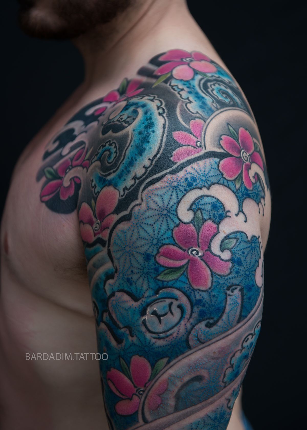 A man has a tattoo of flowers and waves on his arm.