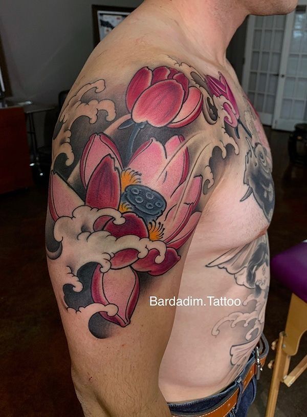 Man's shoulder tattoo: large pink lotus flower, gray and white waves.