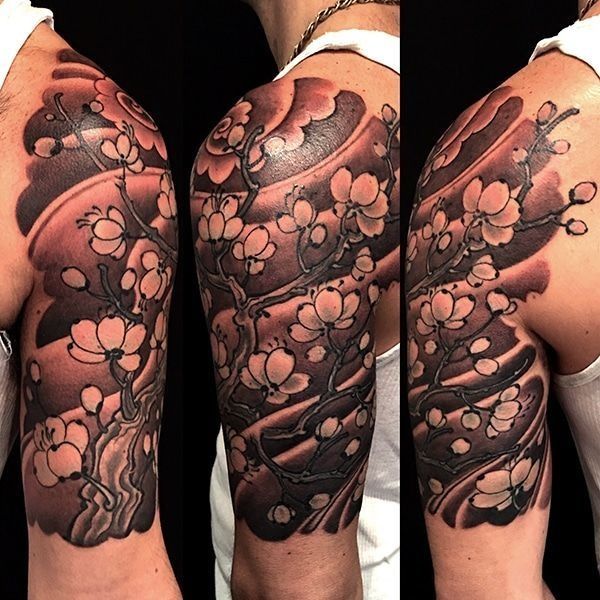 Tattoo of a flowering tree on a person's upper arm. Gray scale blossoms and branches against a shaded background.