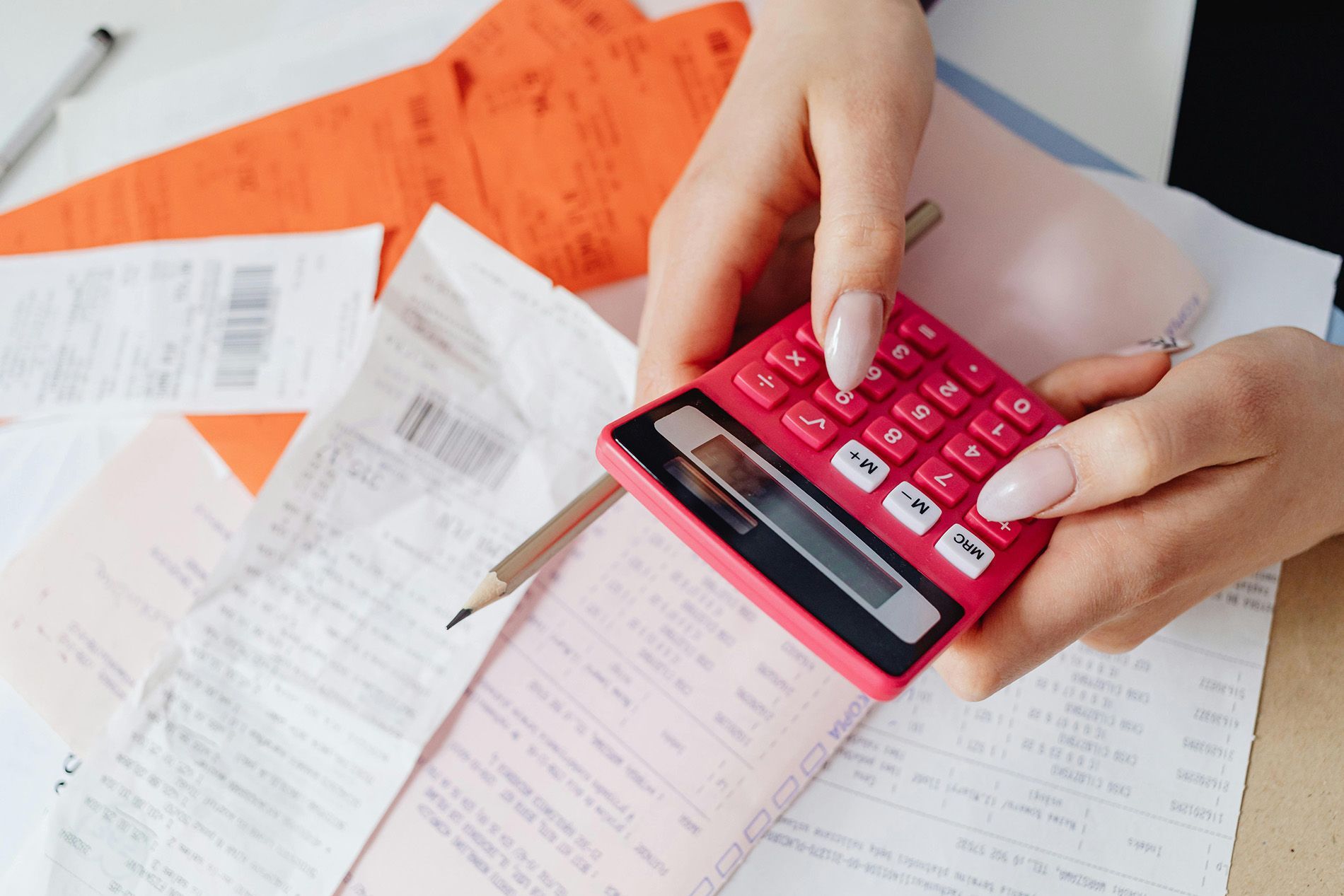 Hands holding a pink calculator surrounded by bills, papers, and a pencil.