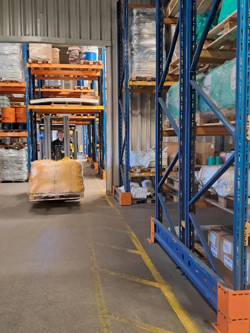 En semitrailer læsset med blåt industrimaskineri inde i et lager. Traileren har hvide sidegardiner med grøn tekst.