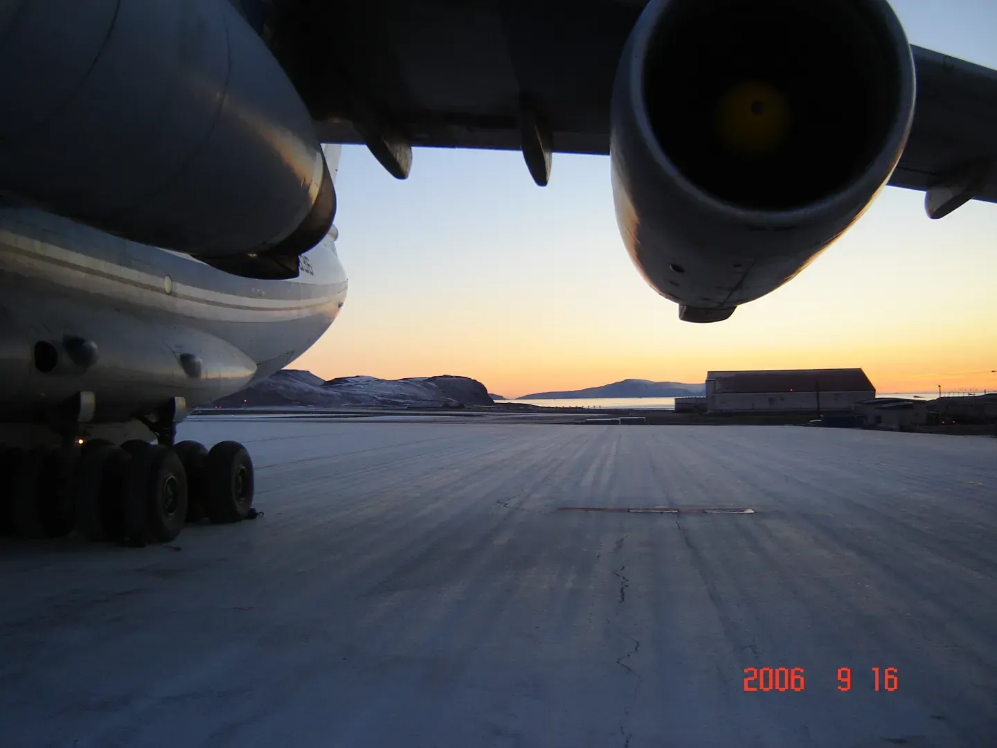 The landing gear and engines of an aircraft parked on an icy, snow-covered tarmac at sunset.