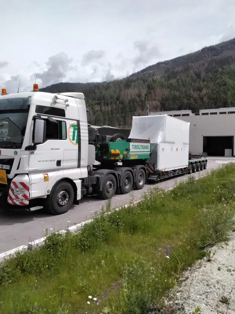 En semitrailer læsset med blåt industrimaskineri inde i et lager. Traileren har hvide sidegardiner med grøn tekst.