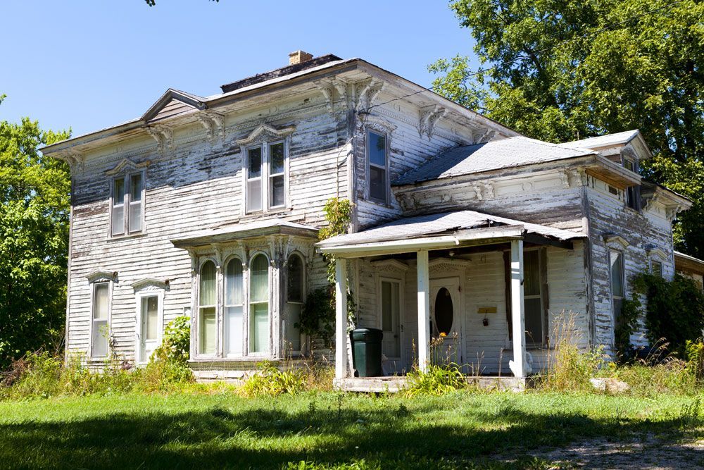 an old white house with a green trash can in front of it