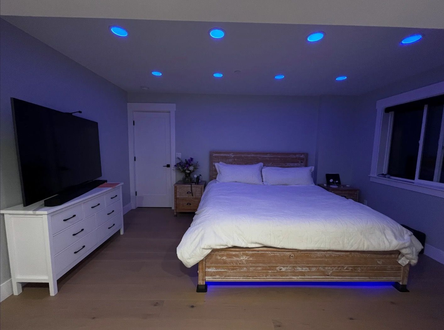A bedroom with a bed , dresser , television and blue lights.