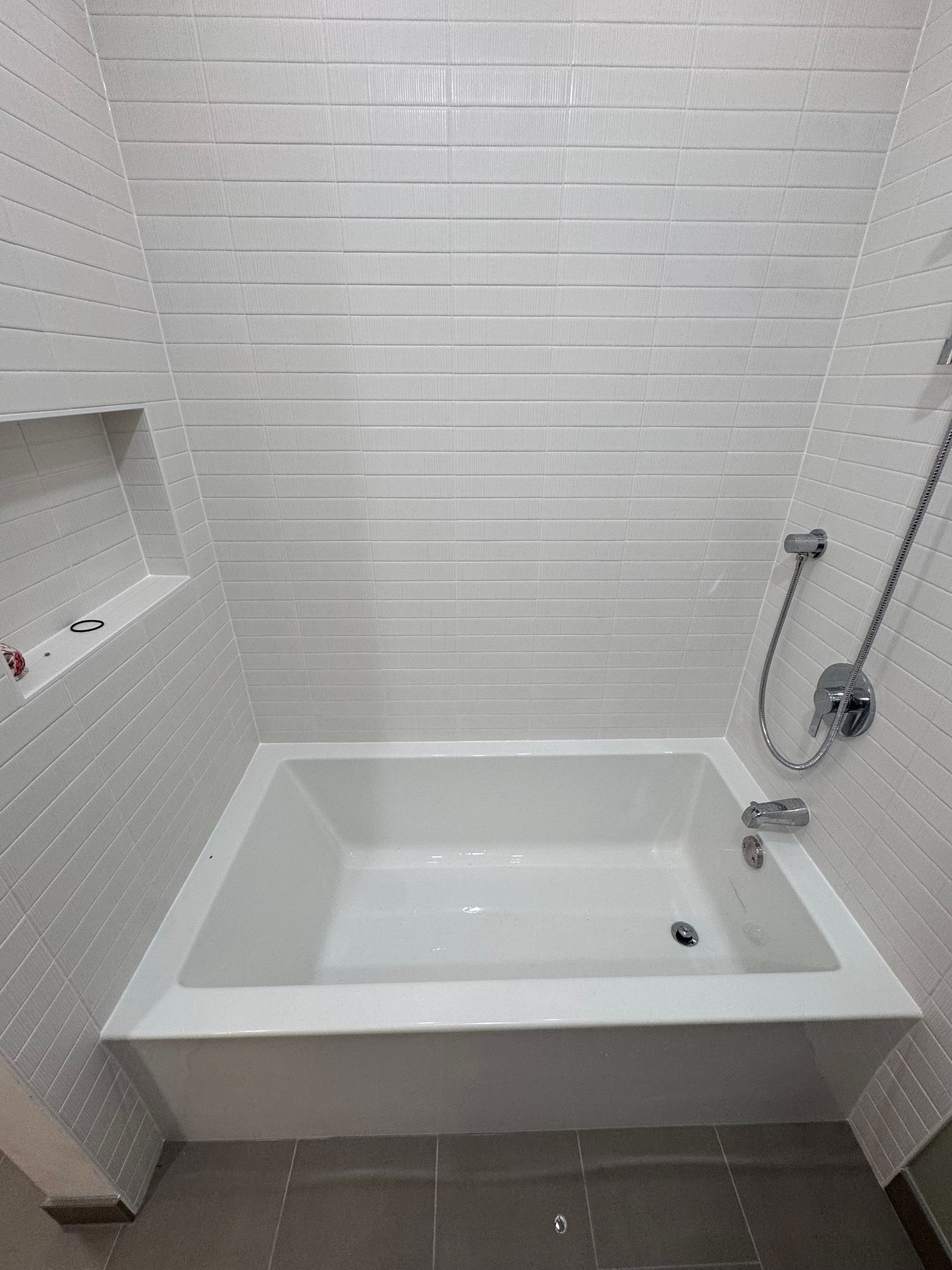 White bathtub in a tiled bathroom with shower fixtures.
