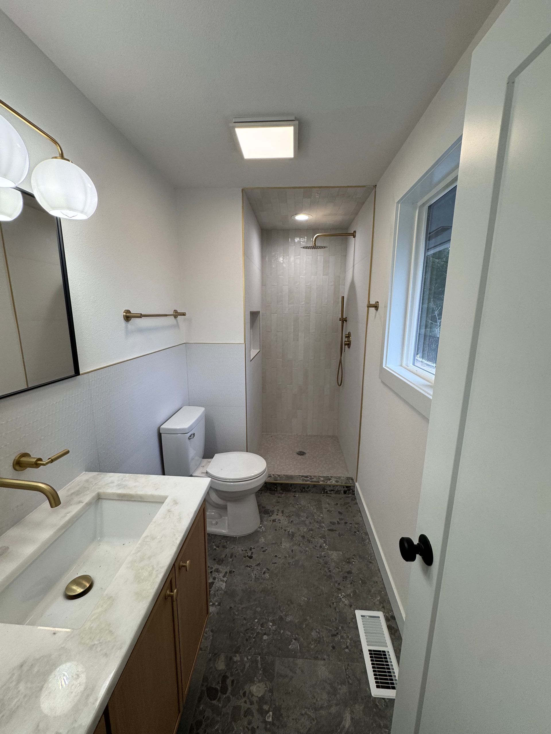 Bathroom with white walls, gold fixtures, and gray flooring; includes a shower, toilet, and vanity.