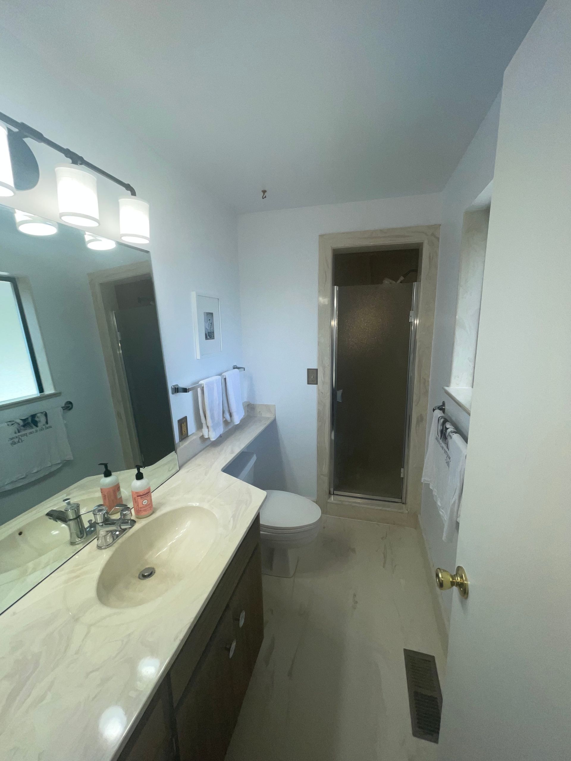 Bathroom with vanity, toilet, and shower. Beige countertop, white walls, and light floor.
