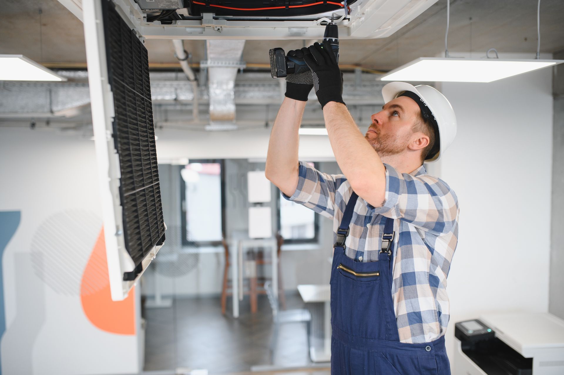 HVAC technician servicing a ceiling-mounted commercial AC unit.