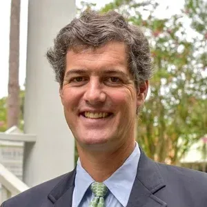 Smiling man in a suit and green tie outdoors with blurred plants in the background