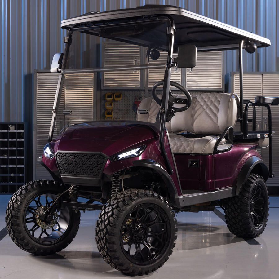 Purple lifted golf cart with black wheels and canopy, parked in a garage.