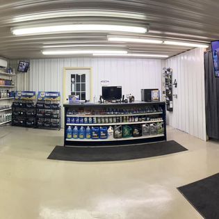 Interior of auto parts store; shelves stocked with products, counter, door, computer, and a TV.