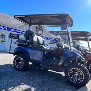 Blue golf cart with black roof, lifted, parked outside a shop.