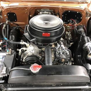 Close-up of a classic car engine in metallic brown; black air cleaner; various components.