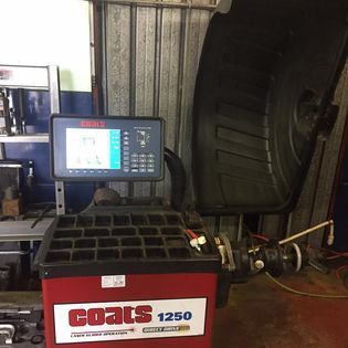 Coats 1250 wheel balancer machine in a repair shop, red and black, with a screen showing tire measurements.