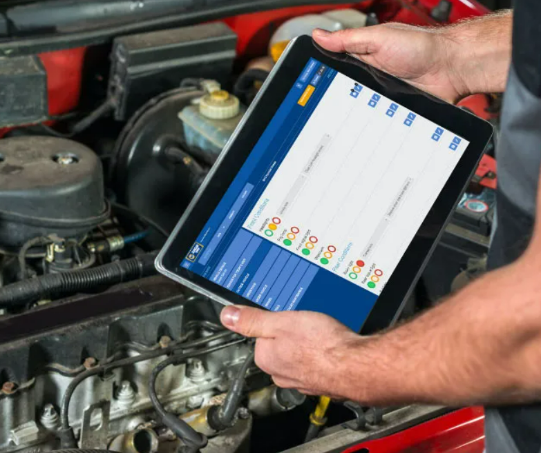 Mechanic holding a tablet displaying car diagnostic data near an open car engine.