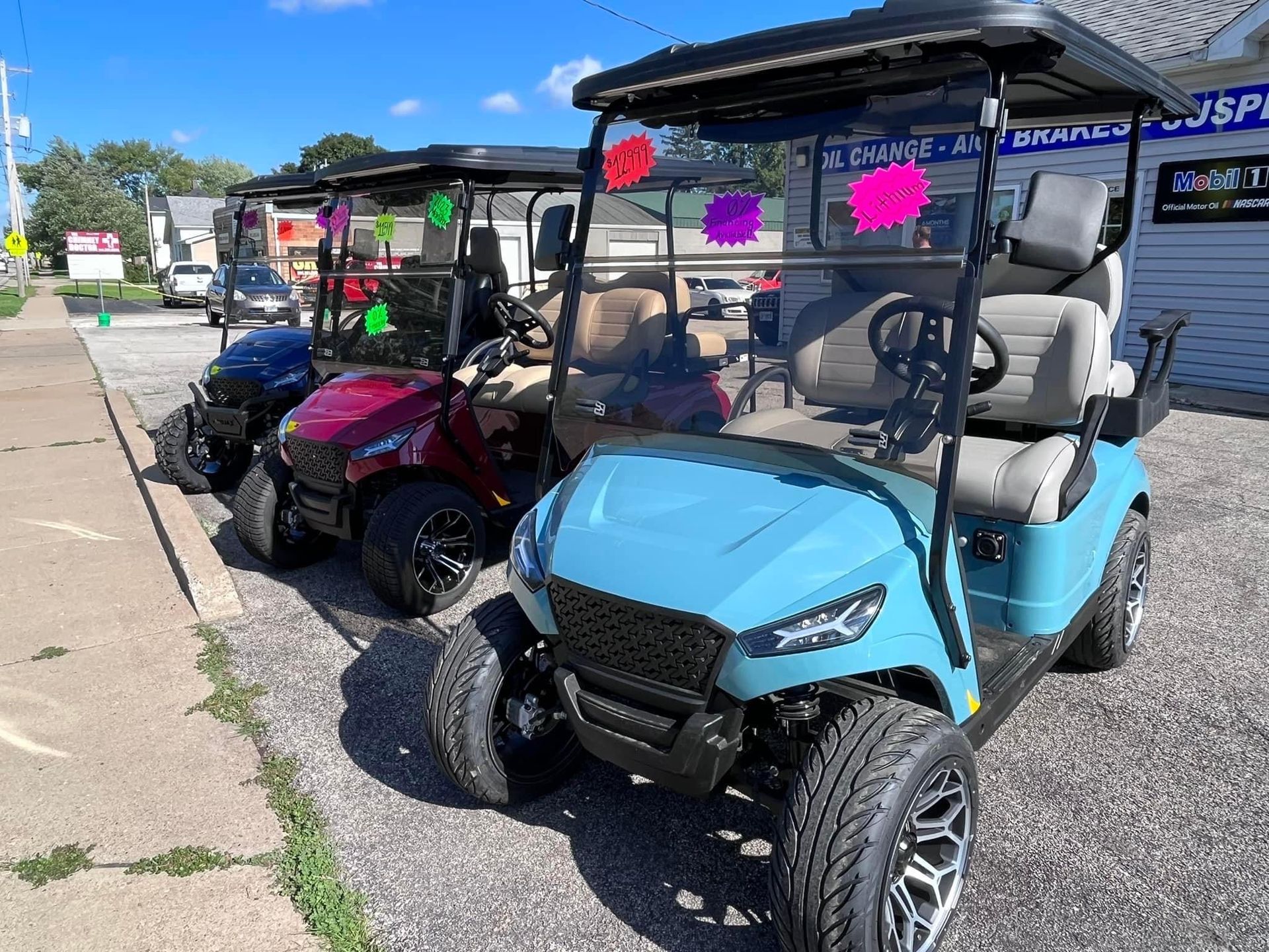 Three golf carts in various colors parked on a sidewalk in front of a store.