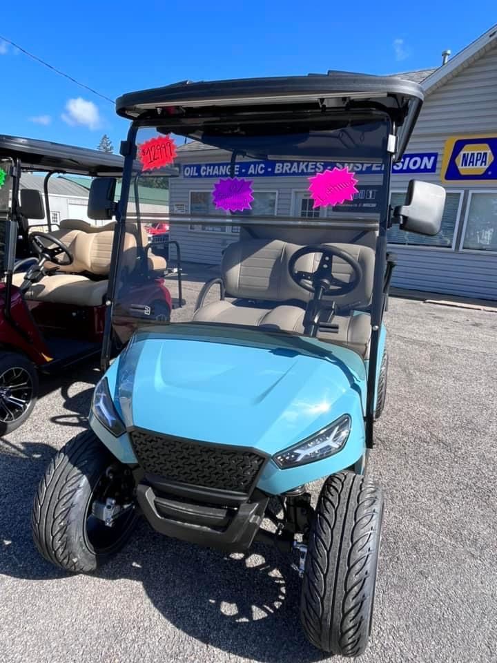 Light blue golf cart with black accents and windshield, parked in front of a building with a Napa Auto Parts sign.