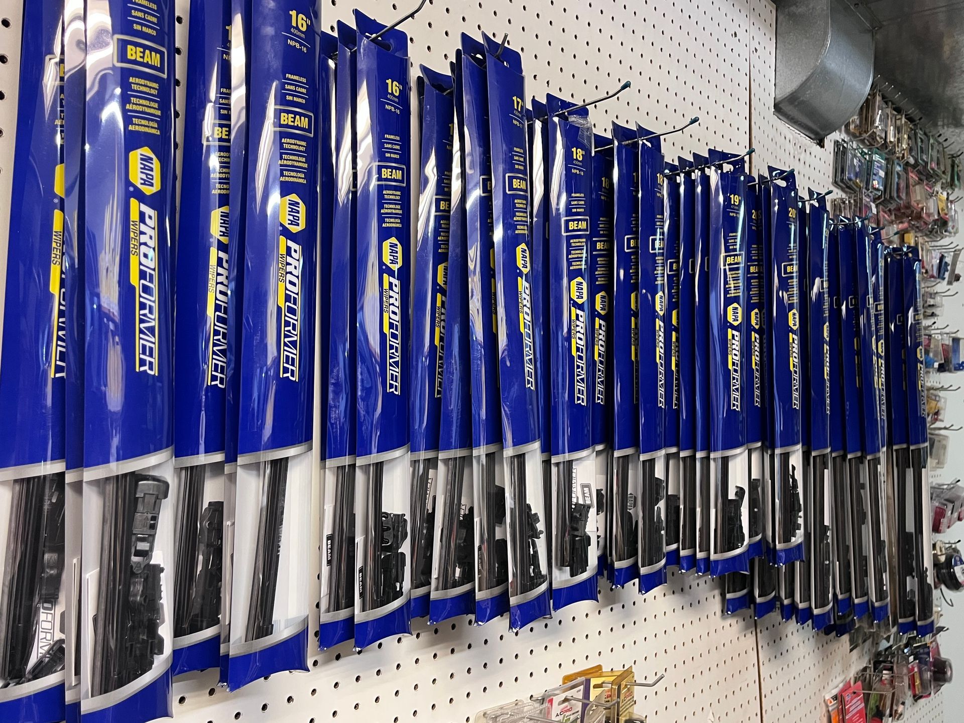 Blue and yellow packaged NAPA wiper blades hanging on a pegboard in a store.