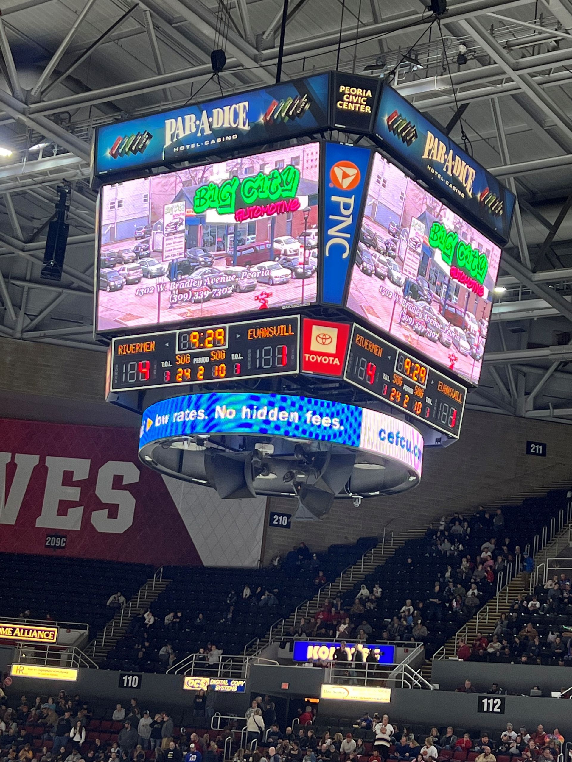 Scoreboard at a sporting event displays scores, team names, and advertisements.
