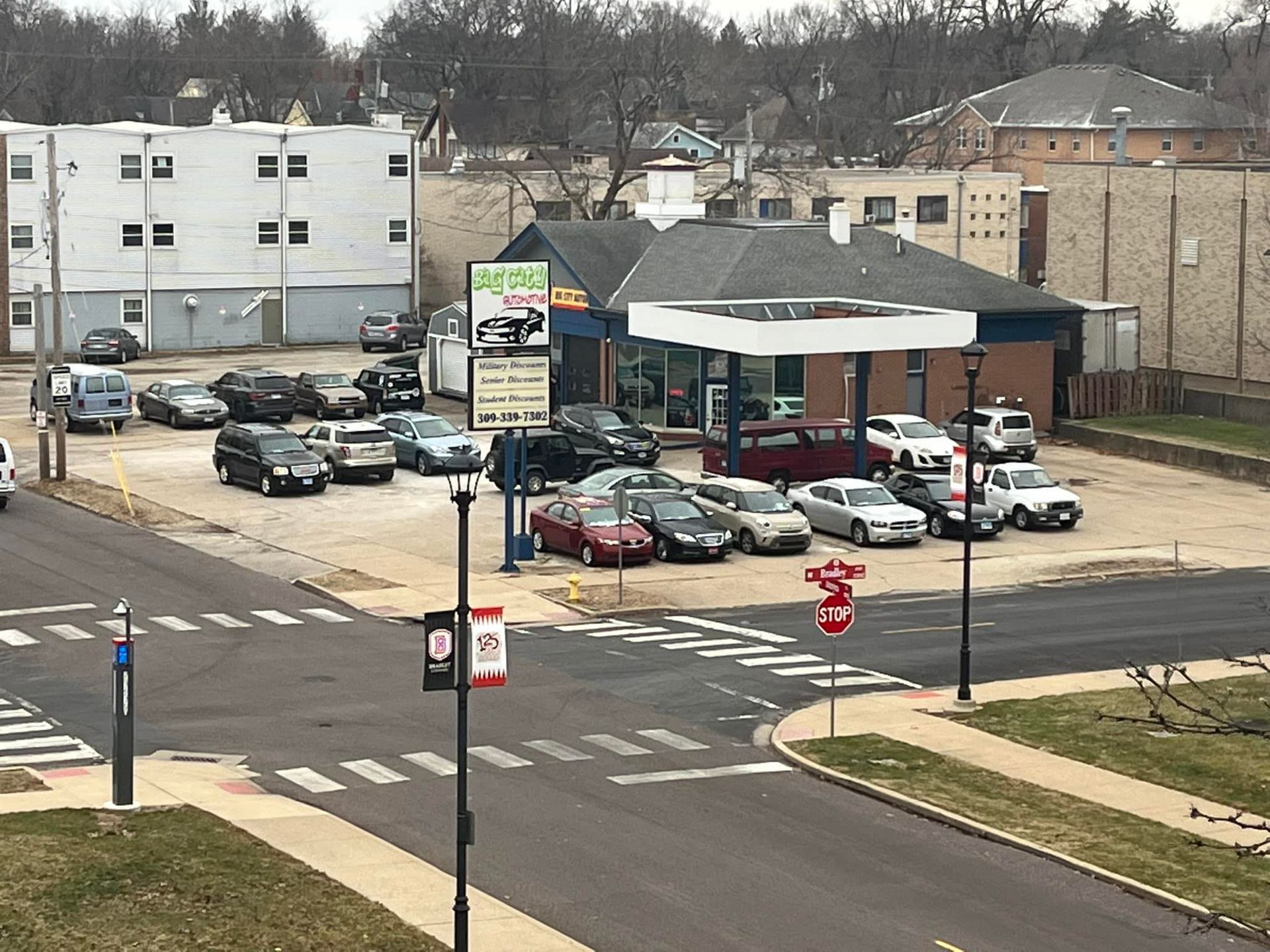 Cars parked at a gas station with a sign, view from an elevated angle across a street intersection.