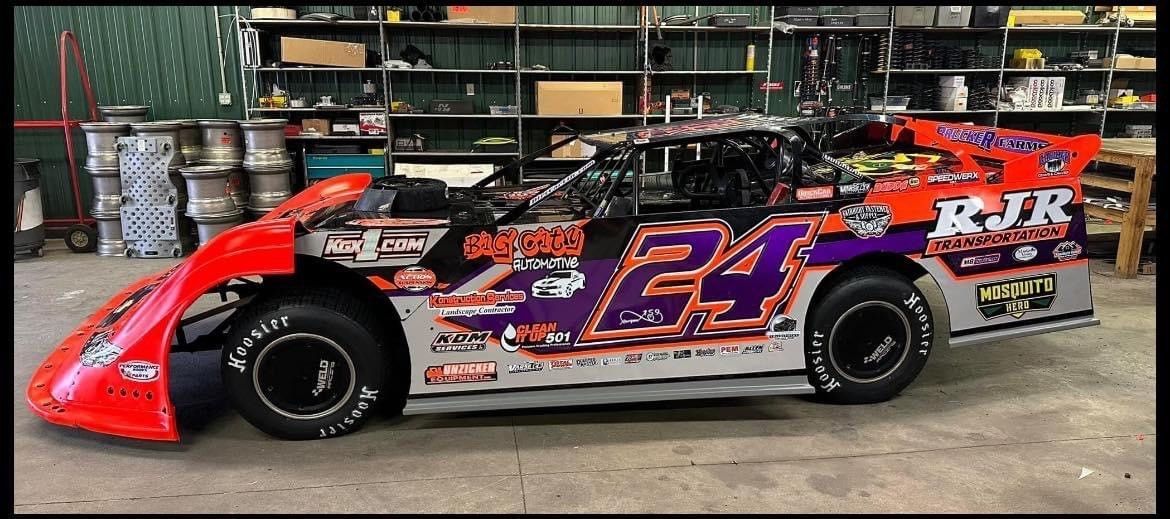 Race car, #24, inside a garage, red and purple accents, KJR racing logo, tires with white lettering.