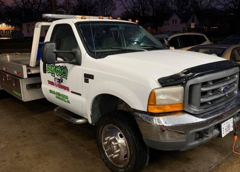 White tow truck parked on a street with the business name 