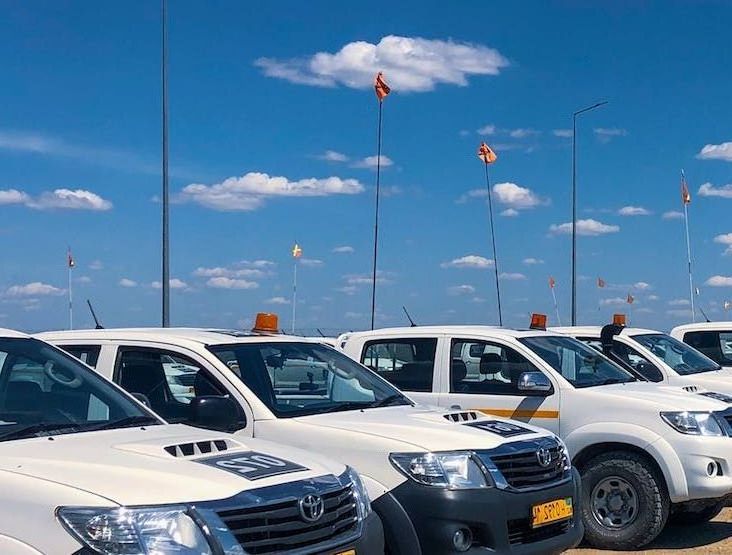 White pickup trucks parked under a blue sky with orange flags and tall poles.