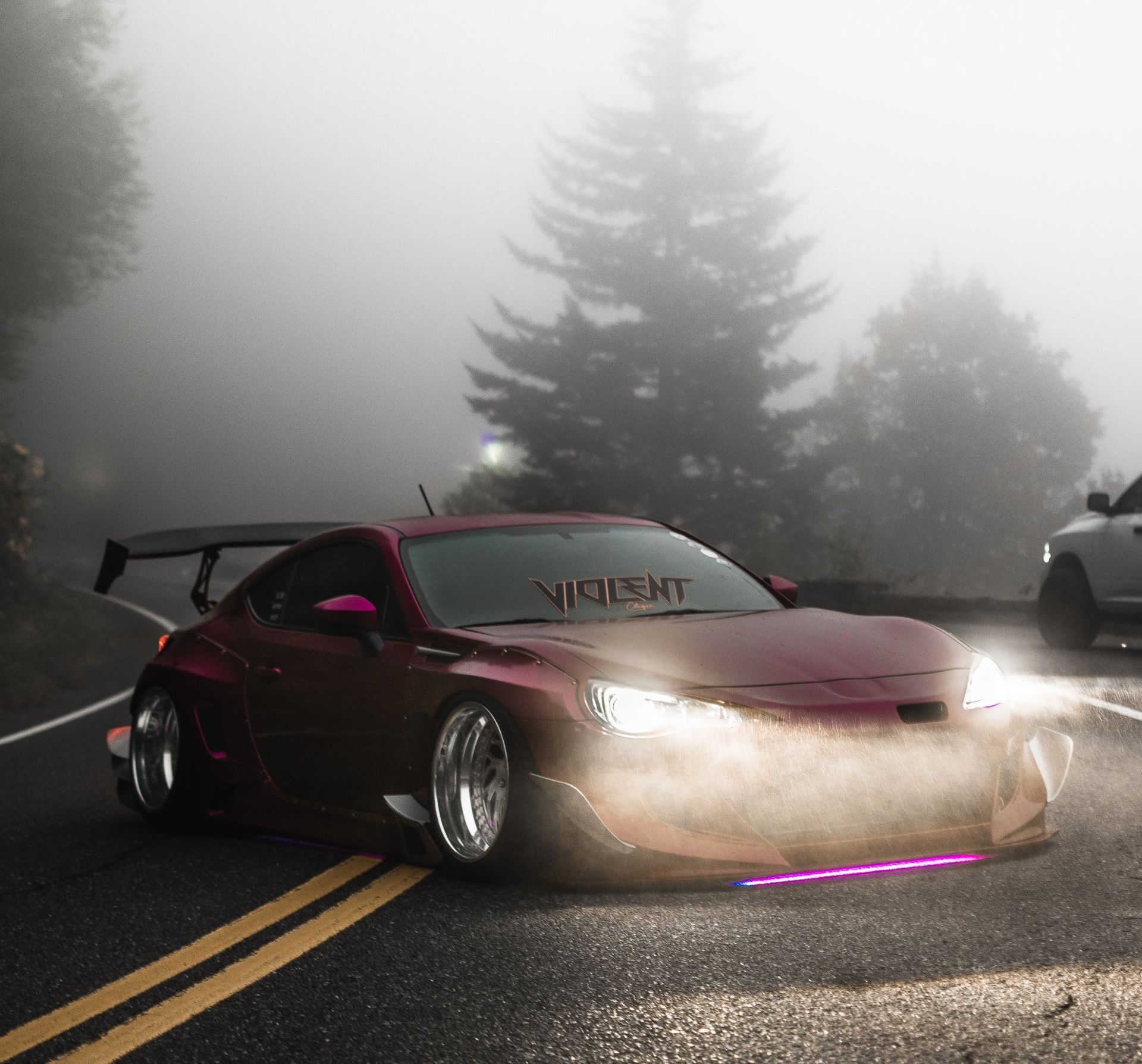 Maroon sports car with a large spoiler driving on a foggy road; 