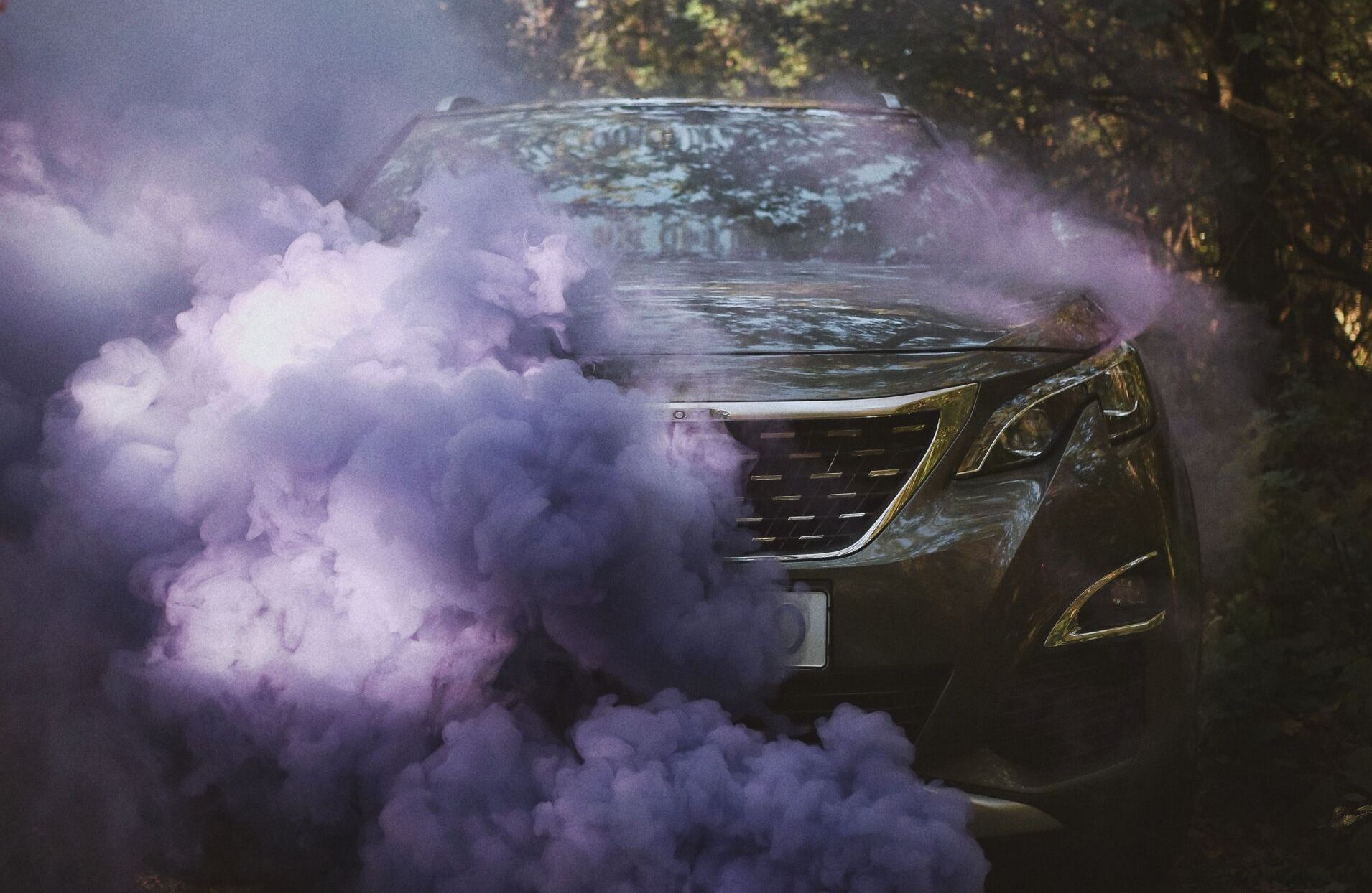 SUV engulfed in purple smoke in a forest setting.