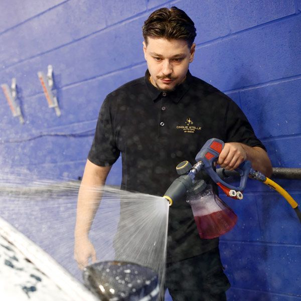 Man spraying a white car with a hose in a blue-walled workshop