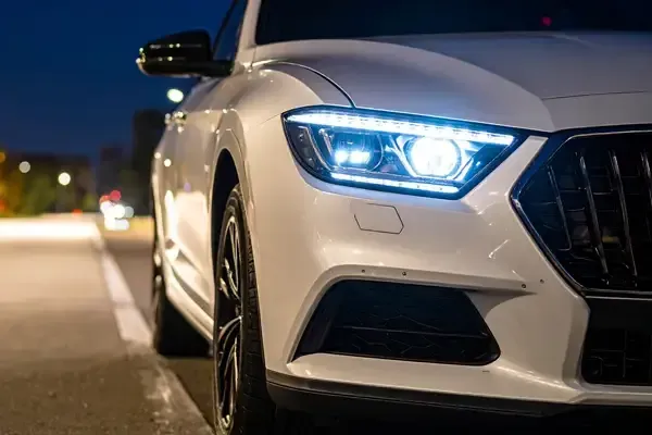 White sedan with bright headlights parked at the curb at night