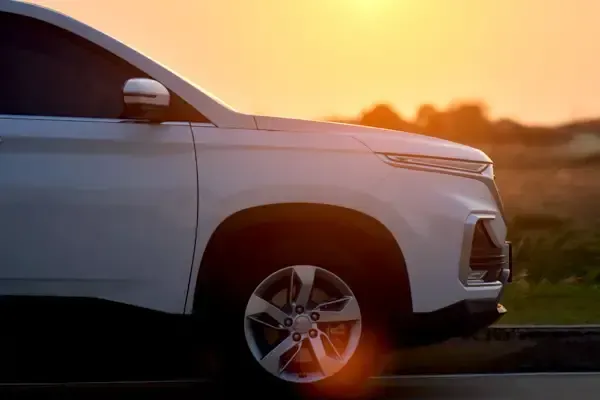 White SUV driving at sunset on a road, side view with warm orange sky