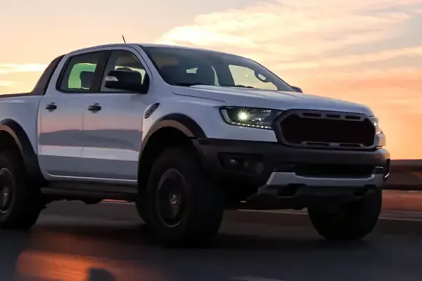 White pickup truck driving on a road at sunset, side view with headlights on