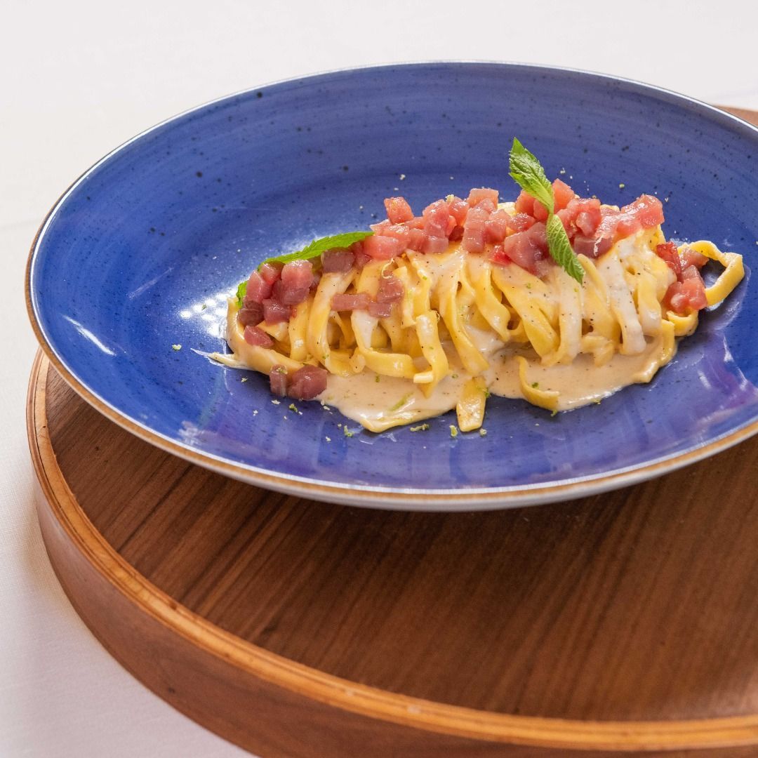 Piatto di pasta in una ciotola blu con vassoio di legno, guarnito con carne.