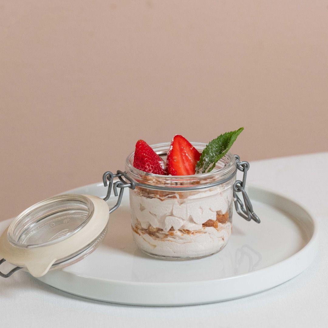 Dessert in barattolo con fragole e una foglia di menta su un piatto bianco.