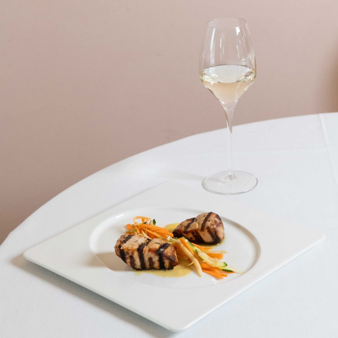 Piatto di cibo grigliato con un bicchiere di vino bianco su una tovaglia bianca.