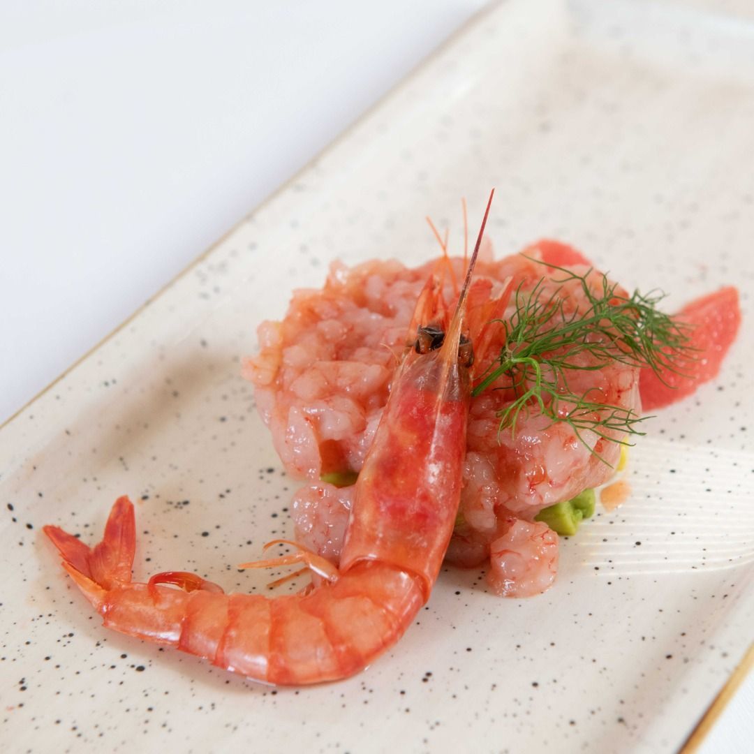 Tartare di gamberi con guarnizione di gamberi interi su un piatto rettangolare.