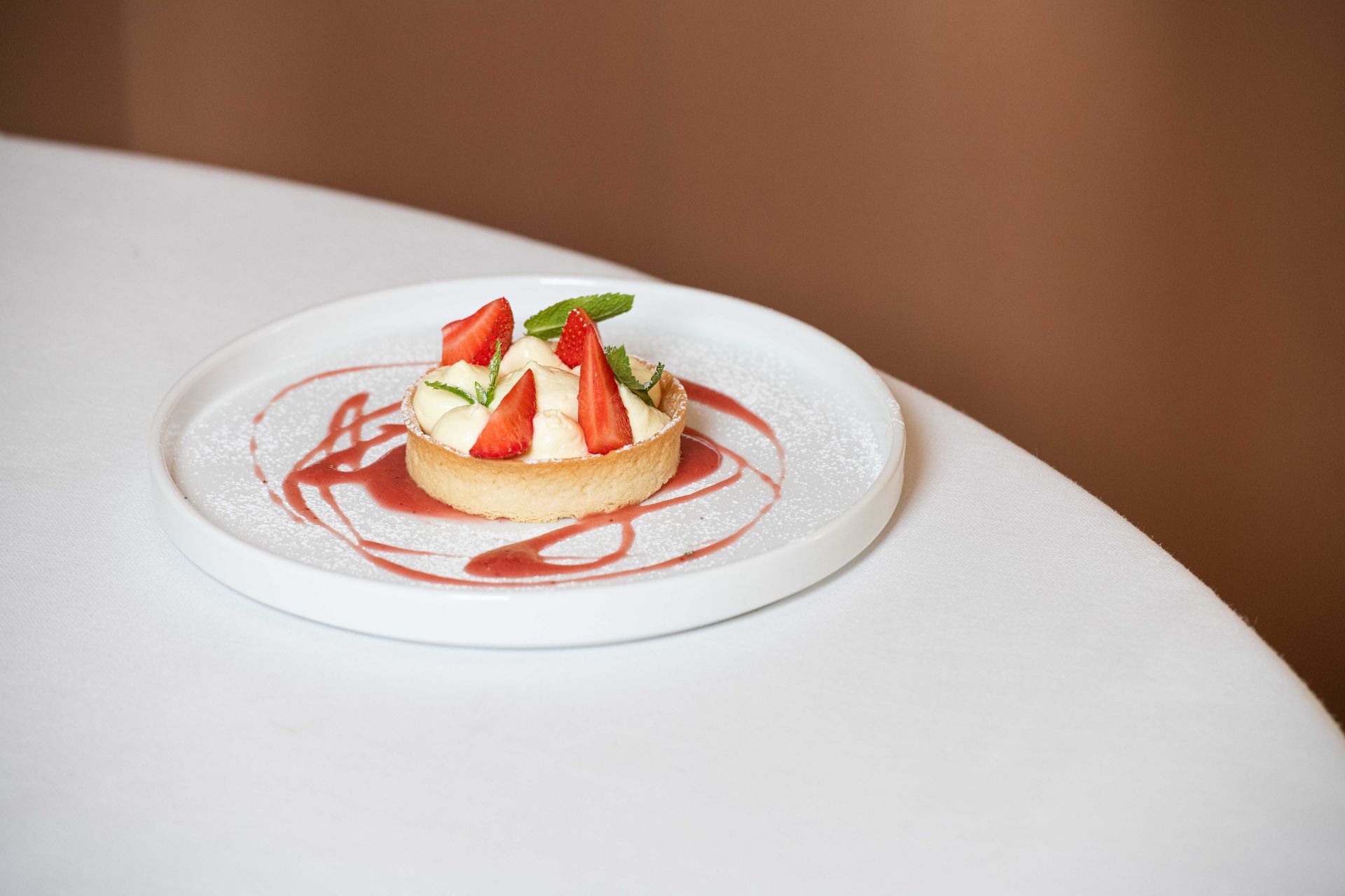 Crostata di fragole su un piatto bianco con vortici di salsa, su un tavolo bianco.