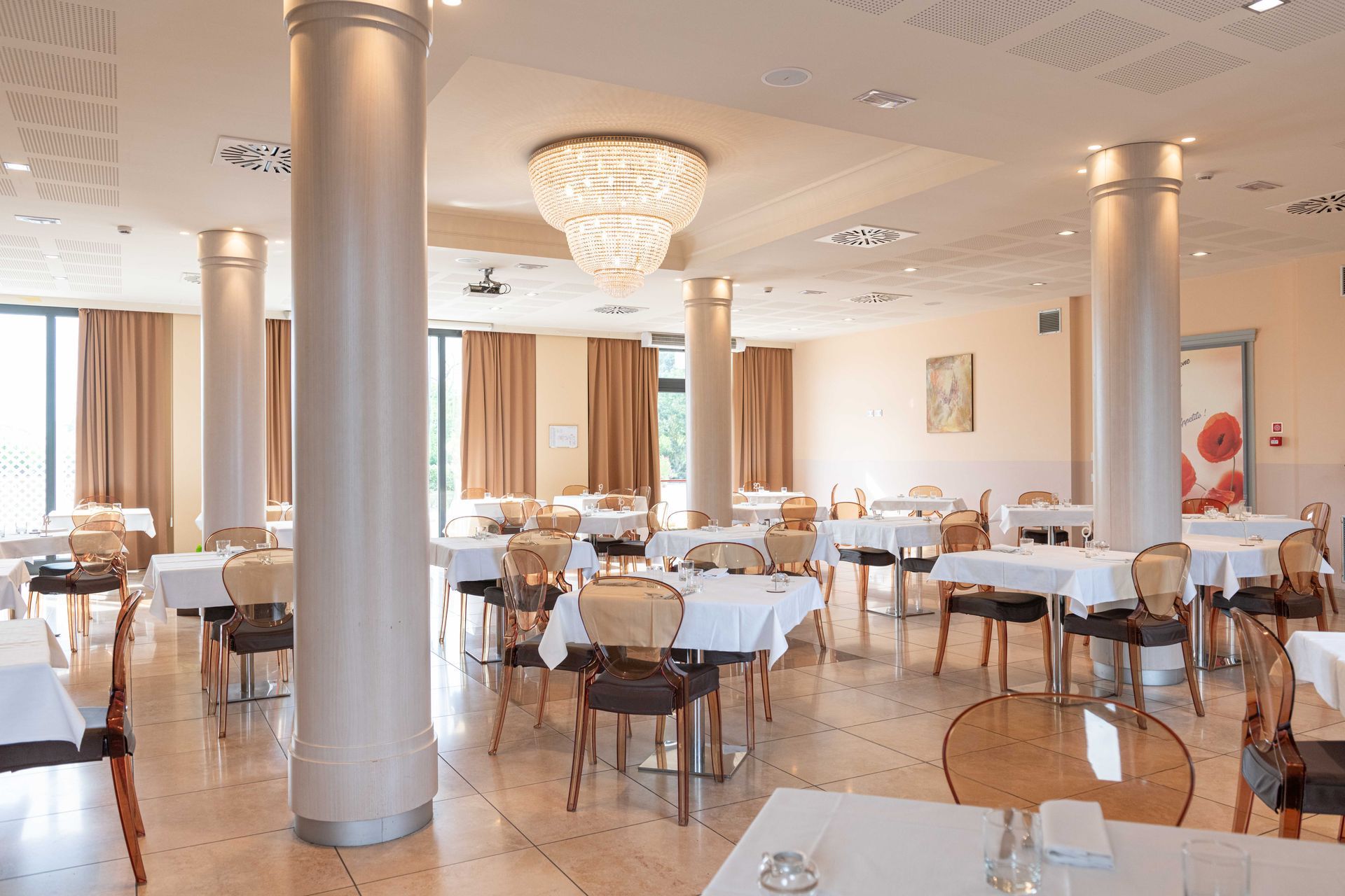 Elegante interno del ristorante con tovaglie, sedie, pilastri e lampadario bianchi.