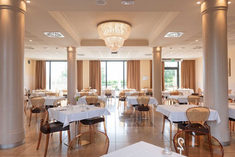 Elegante interno del ristorante con tavoli, sedie, colonne e un lampadario.