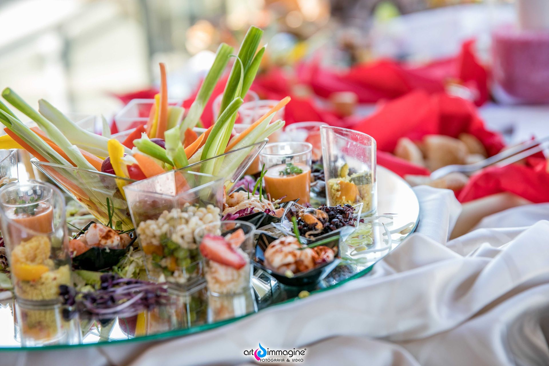 Esposizione di antipasti: verdure, salse e piccole porzioni di cibo in tazze trasparenti su un vassoio riflettente.
