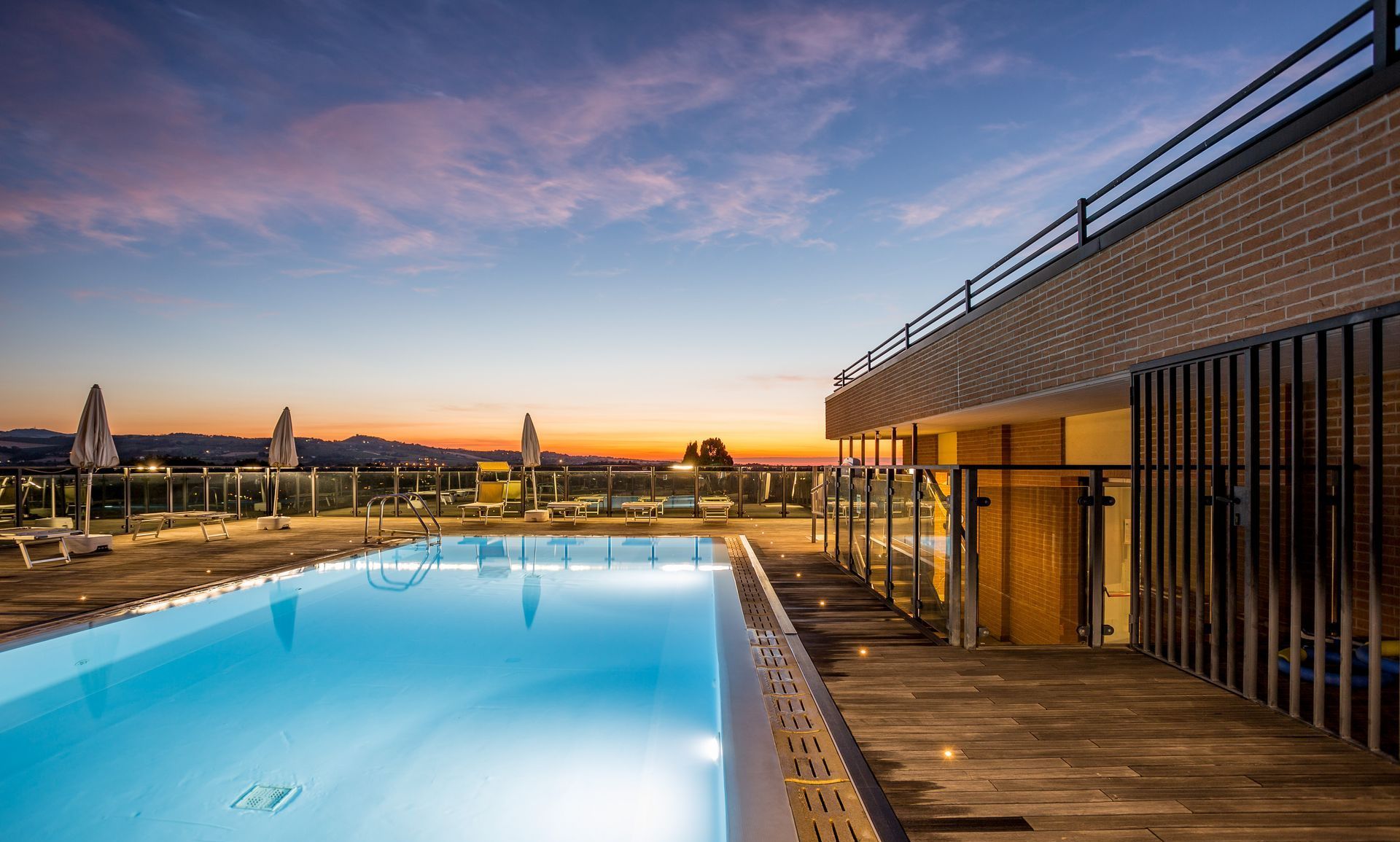 Piscina sul tetto al tramonto, cielo riflesso. Terrazza in legno, edificio con facciata in mattoni.