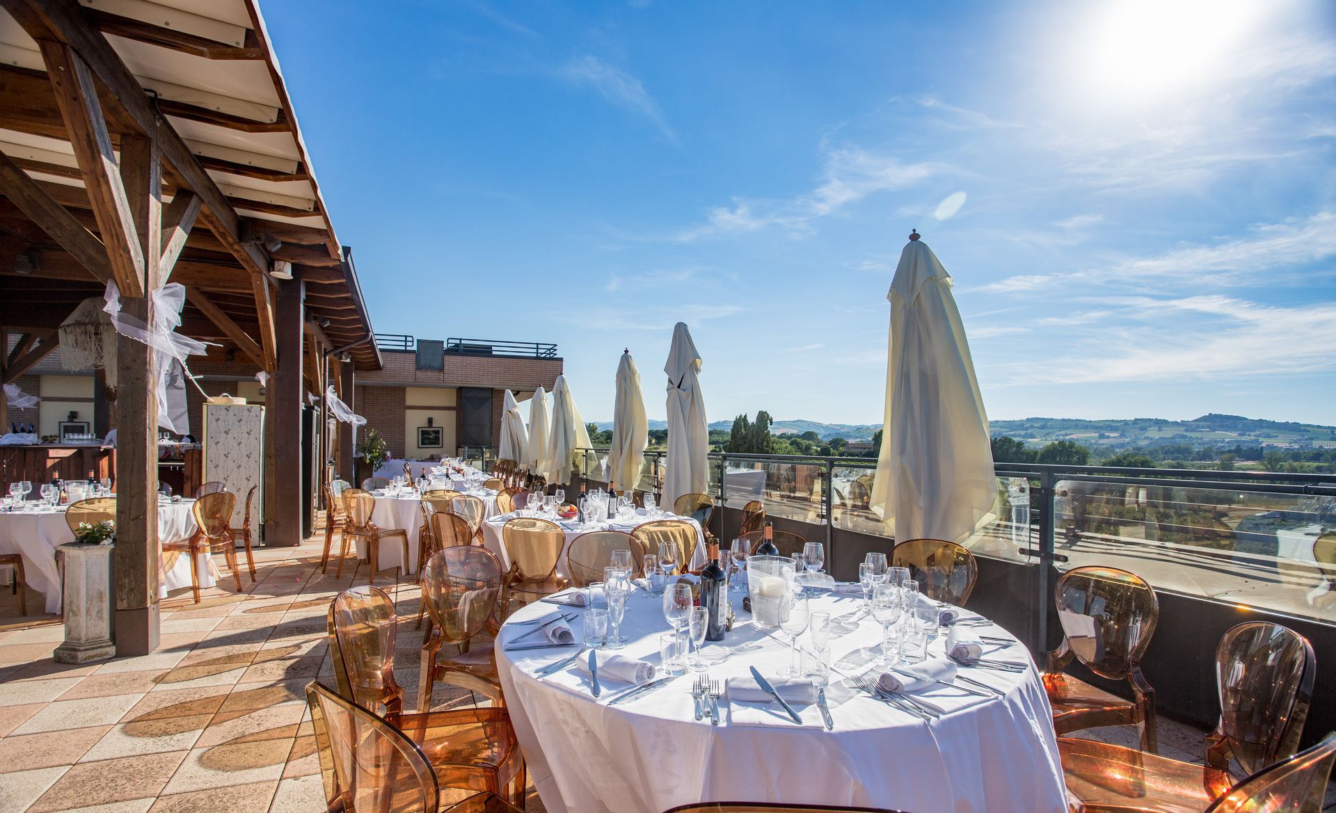Ristorante sul tetto con tavoli apparecchiati per festeggiare, ombrelloni bianchi e cielo azzurro.