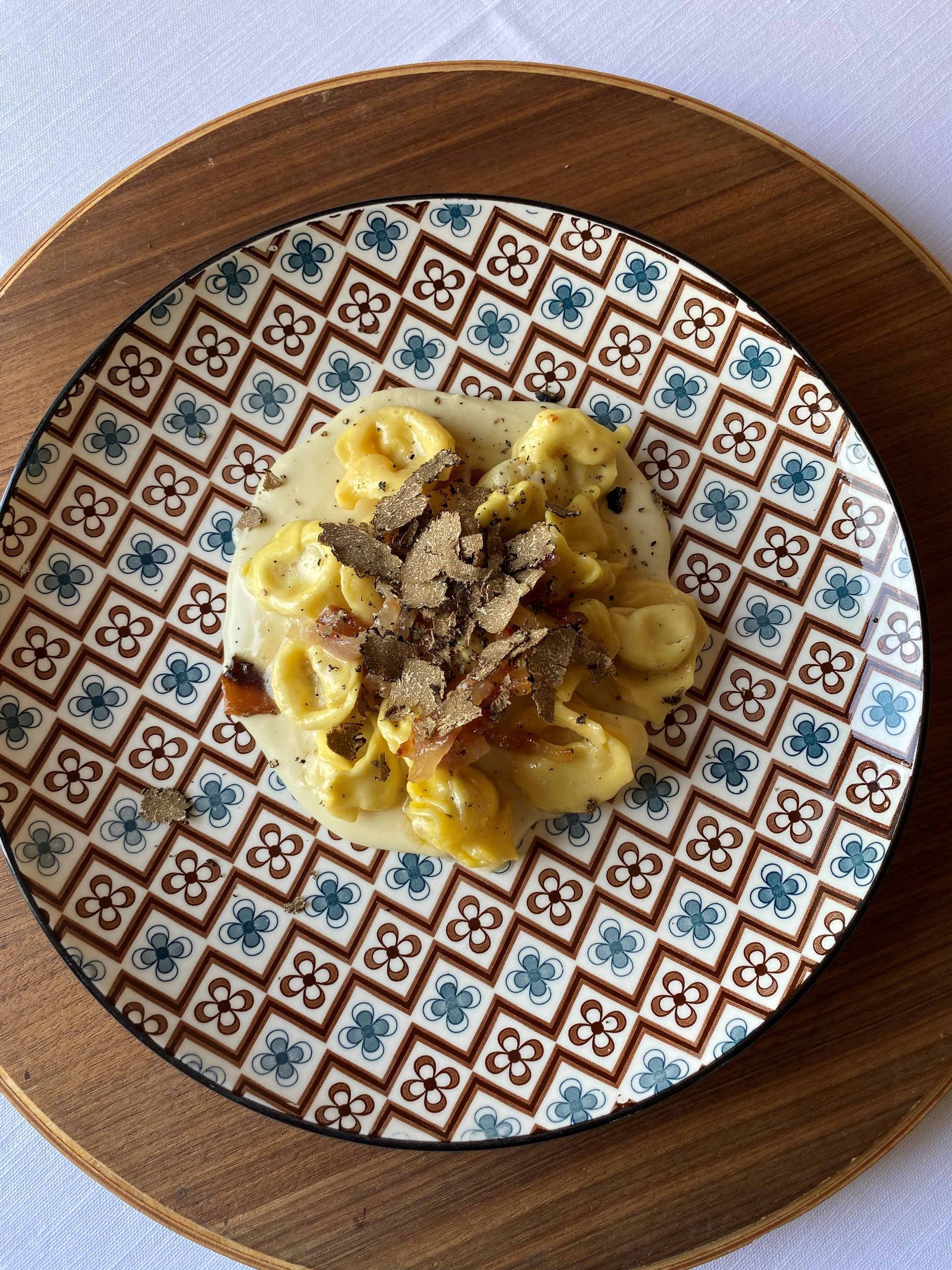 Piatto di pasta con scaglie di tartufo su piatto decorato, vassoio di legno.