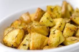 Cubetti di patate arrostite e condite con erbe aromatiche in una ciotola bianca.