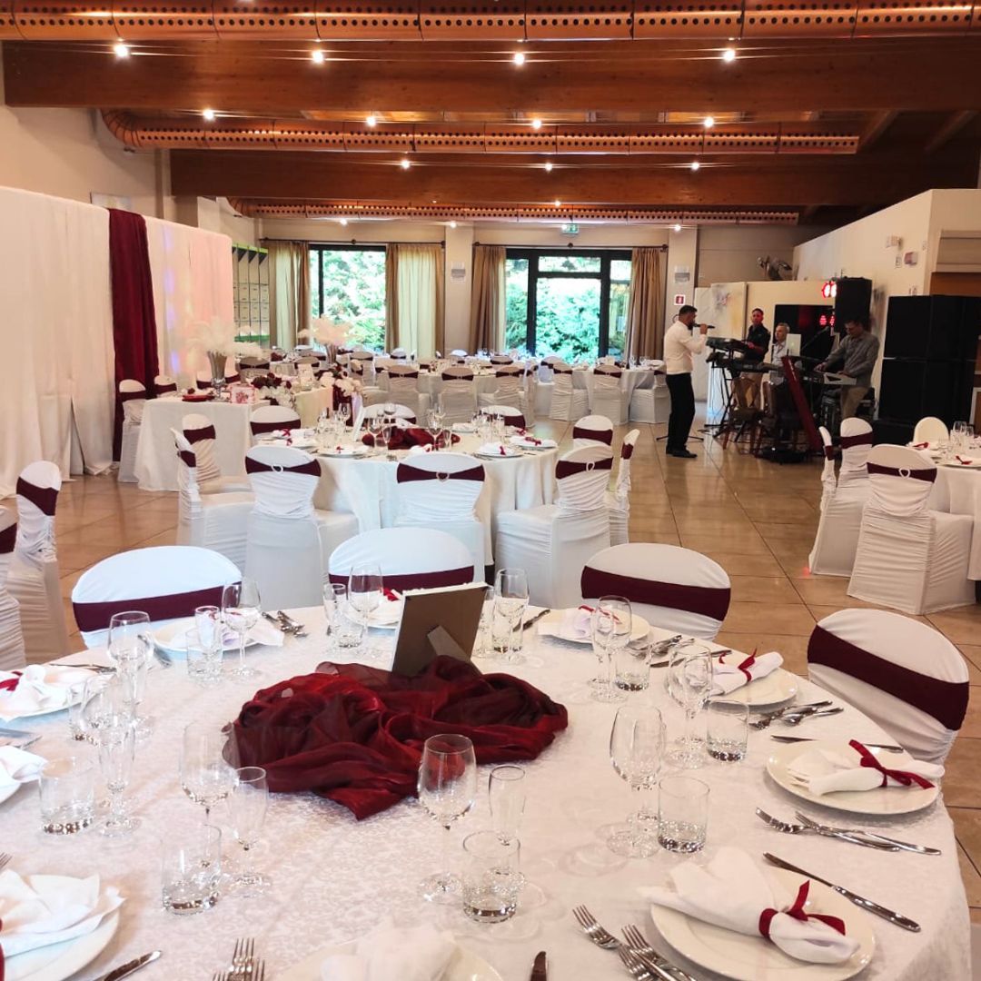 Una sala per banchetti allestita per un evento con tovaglie bianche, dettagli color bordeaux