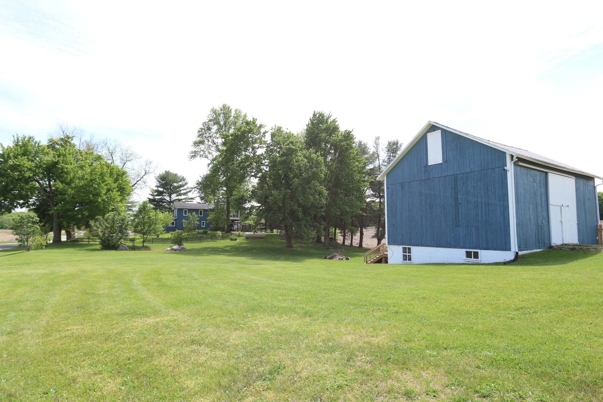 Blue barn and house on a green field under a clear sky.
