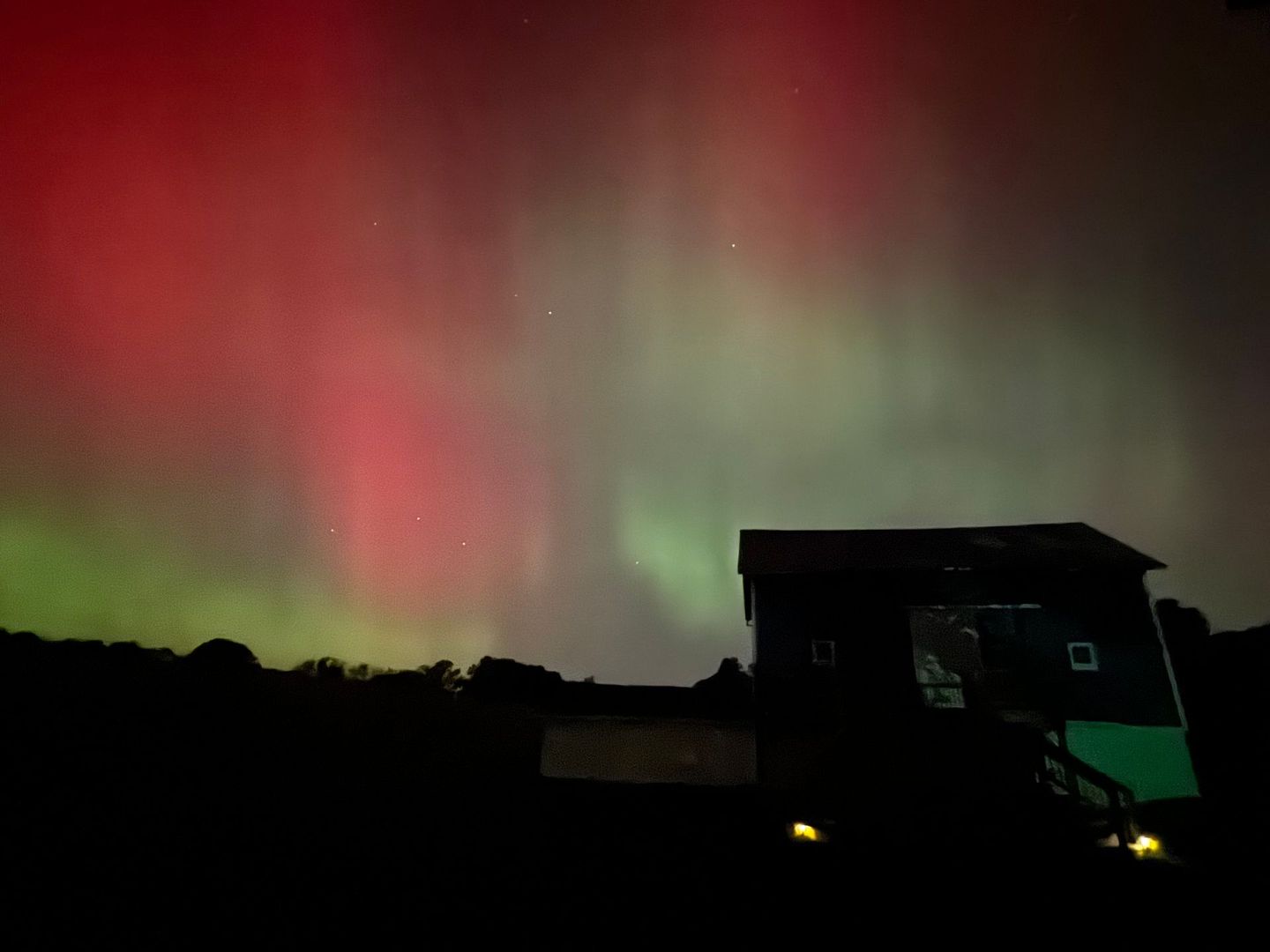 Aurora borealis over Inn Between the Lakes wedding venue barn with a green glow, red sky.