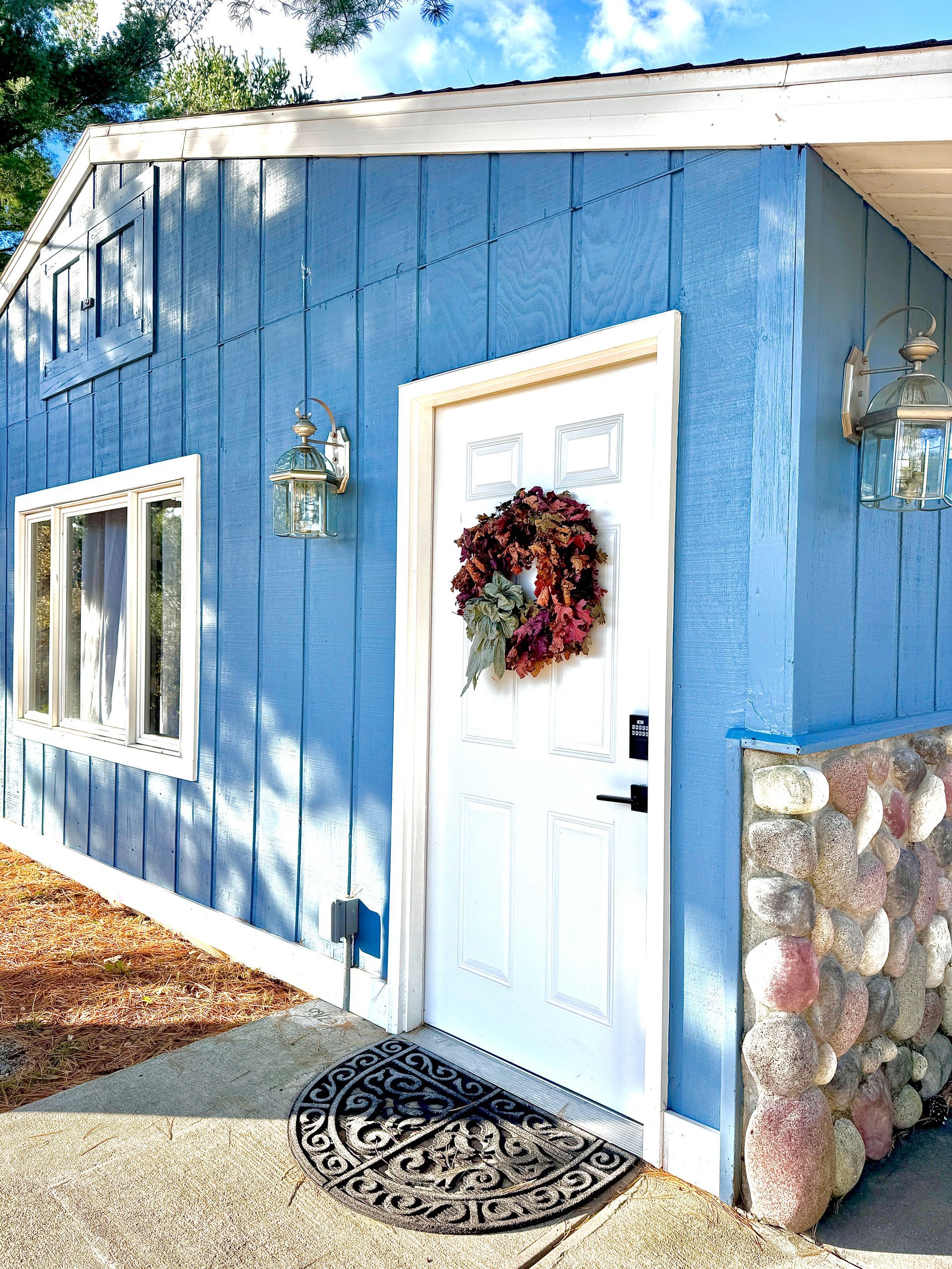Blue building with white door and wreath, stone base, and two wall lamps.